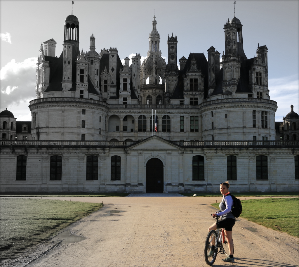 a woman on her bike in front of the entrance of chambord castle