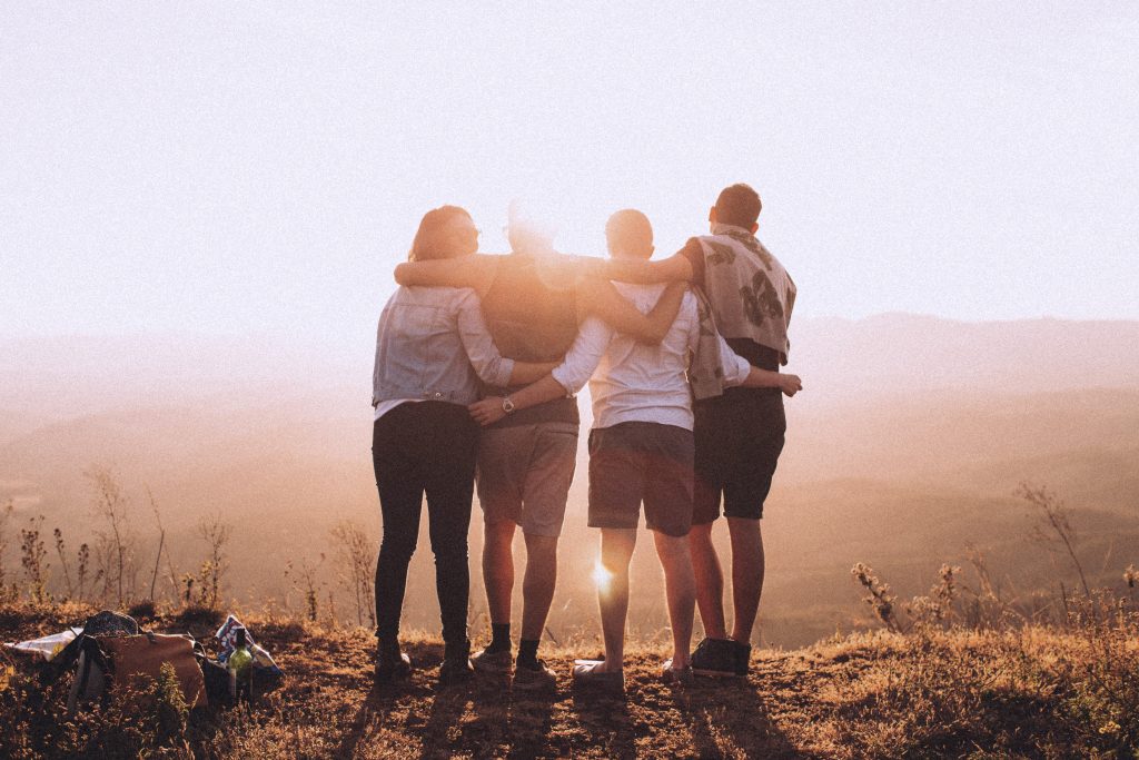 four people holding arms and shoulders in front of the sunrise