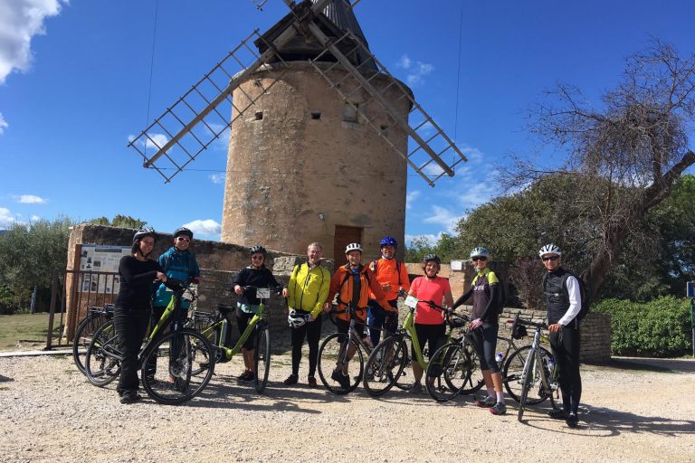 a group of people in front of a mill on their e-bike in provence